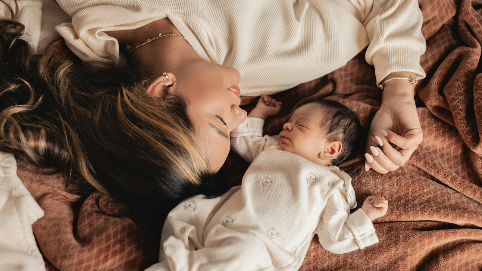 Moeder ligt naast pasgeboren baby in zachte Nuvino Kids babykleding