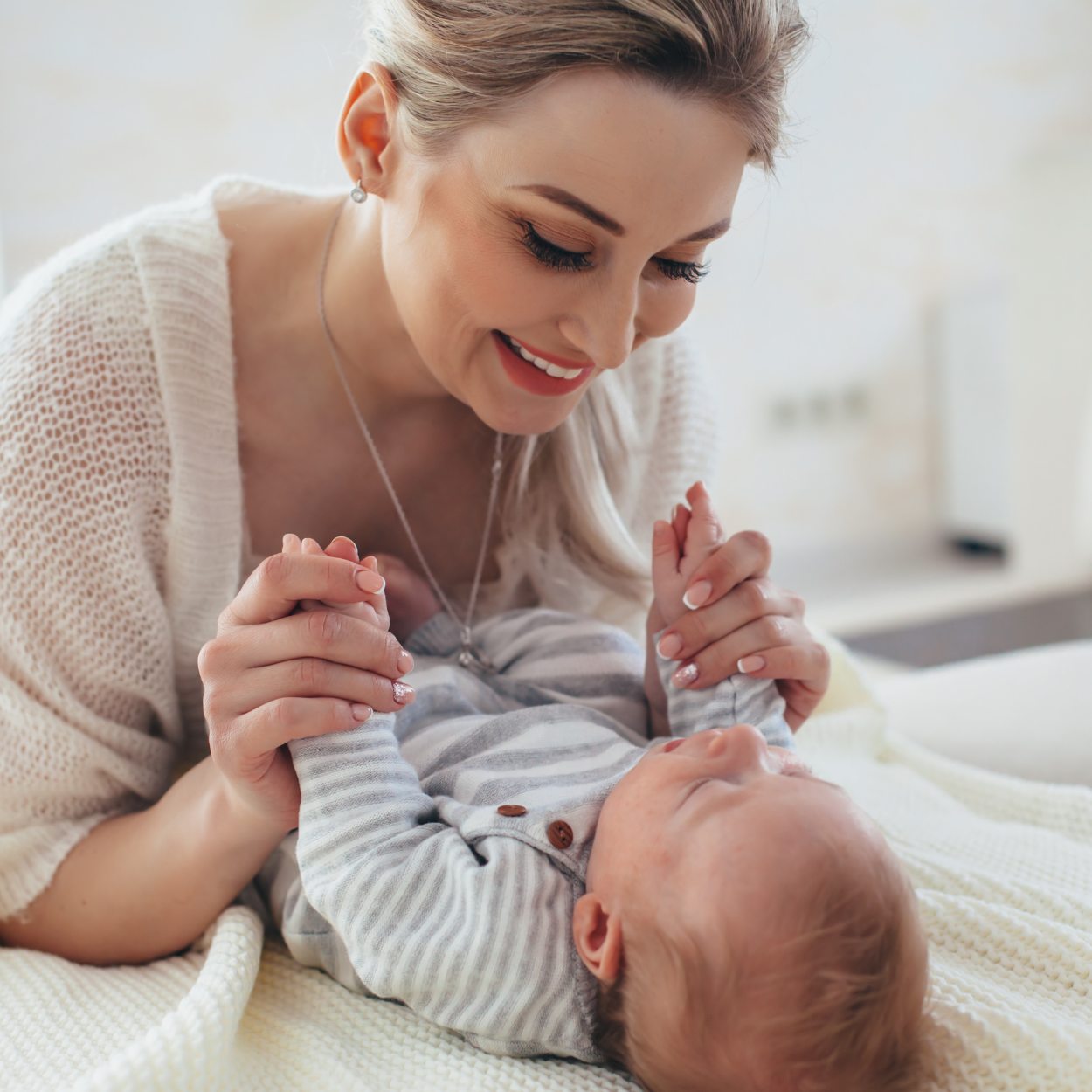 Moeder speelt liefdevol met baby op zachte witte deken