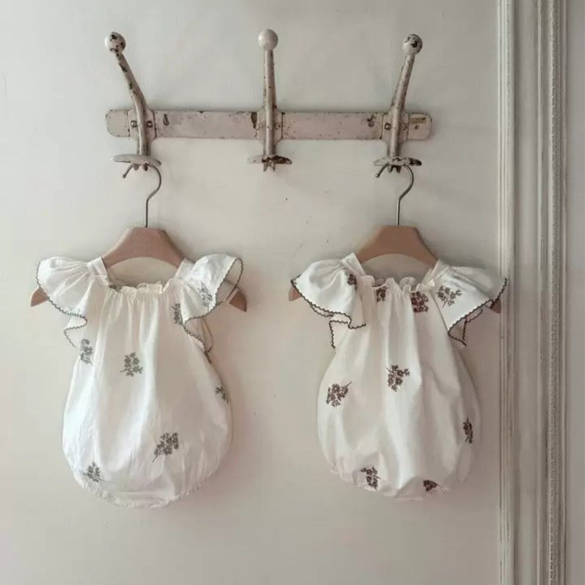 Baby zomerromper met bloemenborduursel, flutter mouwen en effen ontwerp in de kleuren groen en coffee, flatlay gefotografeerd op een lichte achtergrond.