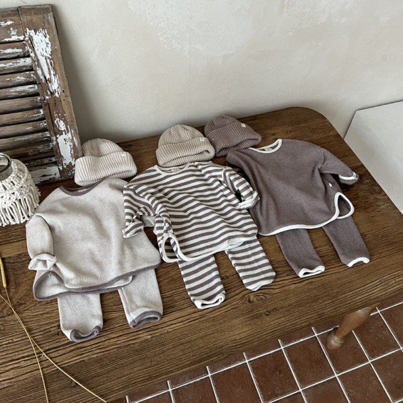 Tweedelige unisex waffle lounge set met losse top en bijpassende broek in neutrale kleuren grijs, bruin en coffee, flatlay gepresenteerd op een lichte achtergrond.