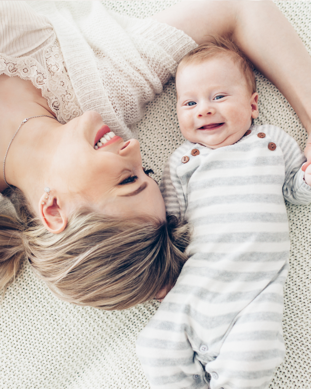 Woman and baby lying on a textured surface, both smiling.