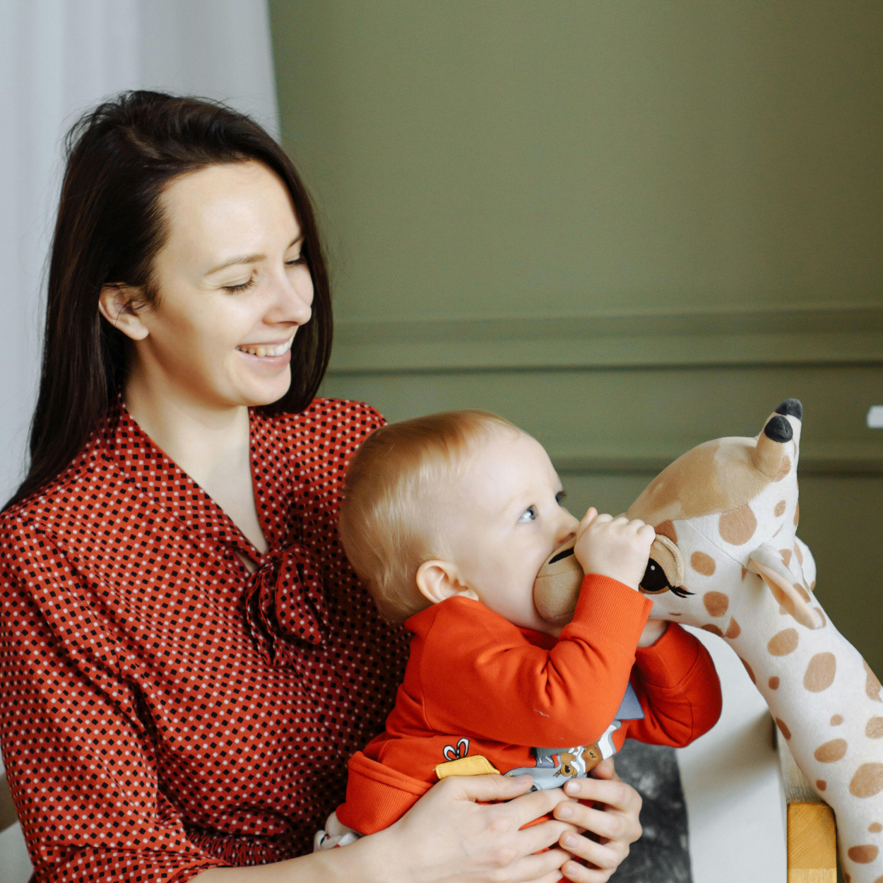 Woman holding a baby with a plush deer toy in a home setting